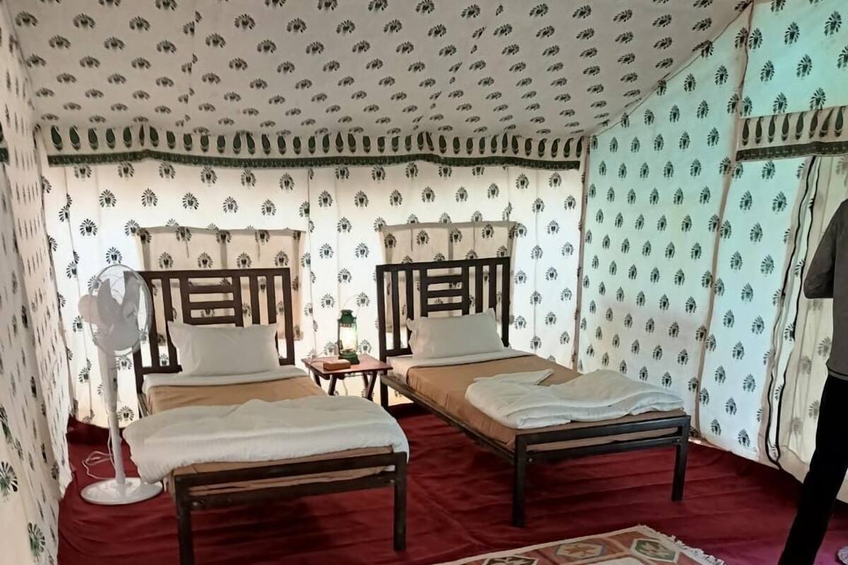 Une chambre avec deux lits en bois, une moquette rouge et un papier peint à motifs.