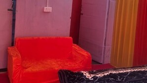 Een kamer met een rode bank, een bed met een wit laken en een geel hemeltje.