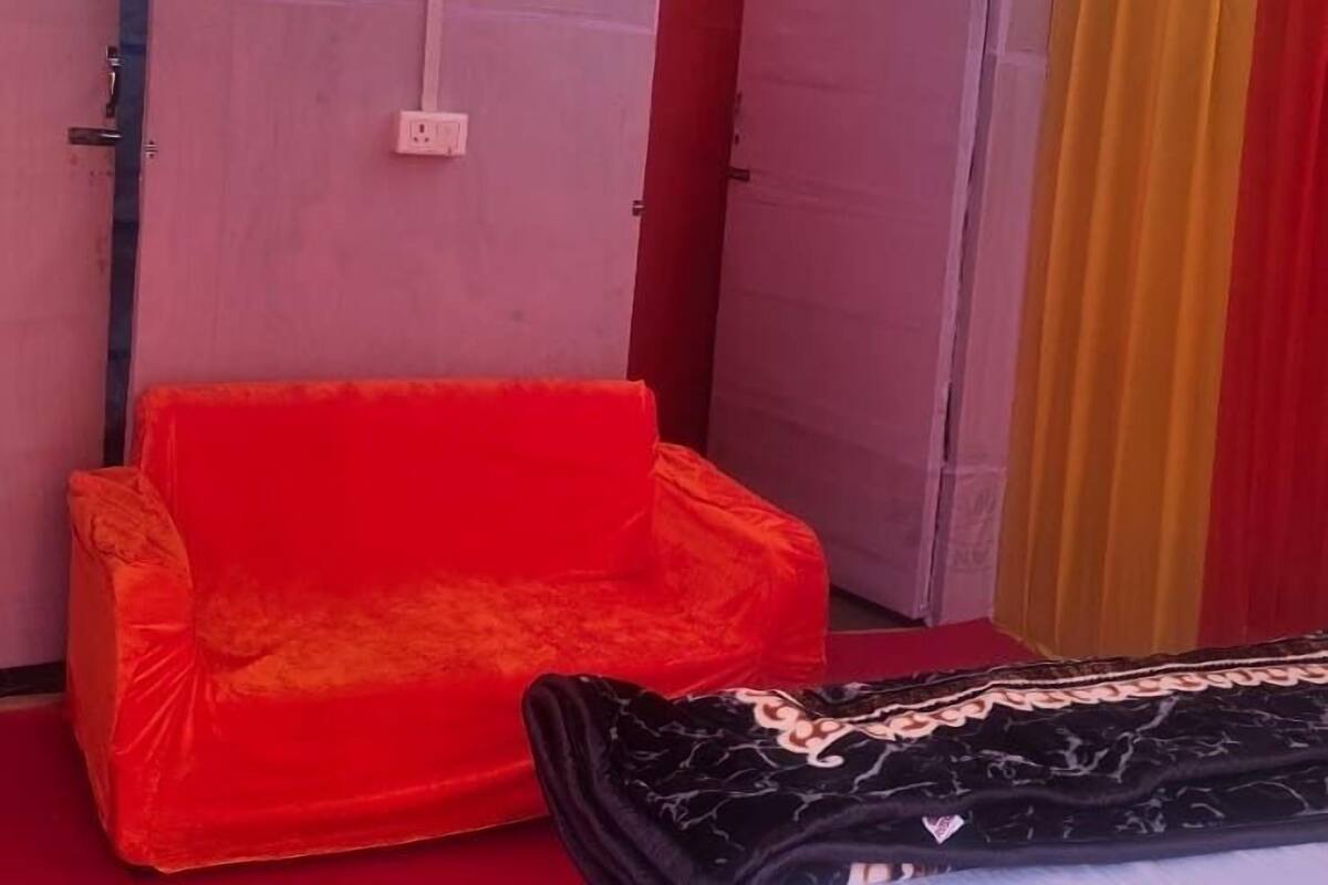 Une pièce avec un canapé rouge, un lit recouvert d’un drap blanc et un baldaquin jaune.