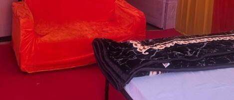 A room with a red sofa, a bed with a white sheet, and a yellow canopy.