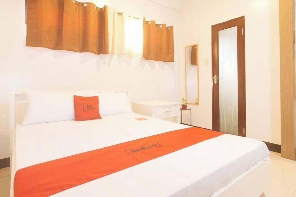 Una habitación de hotel con una cama, una mesita de noche, un espejo y una puerta.