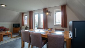A dining area with a wooden table, four chairs, a bowl of fruit, and a television on a cabinet.