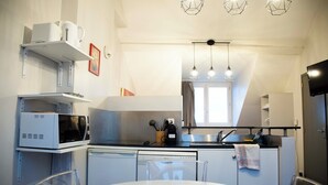 A compact kitchen with white appliances, a dining table, and pendant lighting. - Smart Appart Cherbourg La Rose des vents (Cherbourg-en-Cotentin)