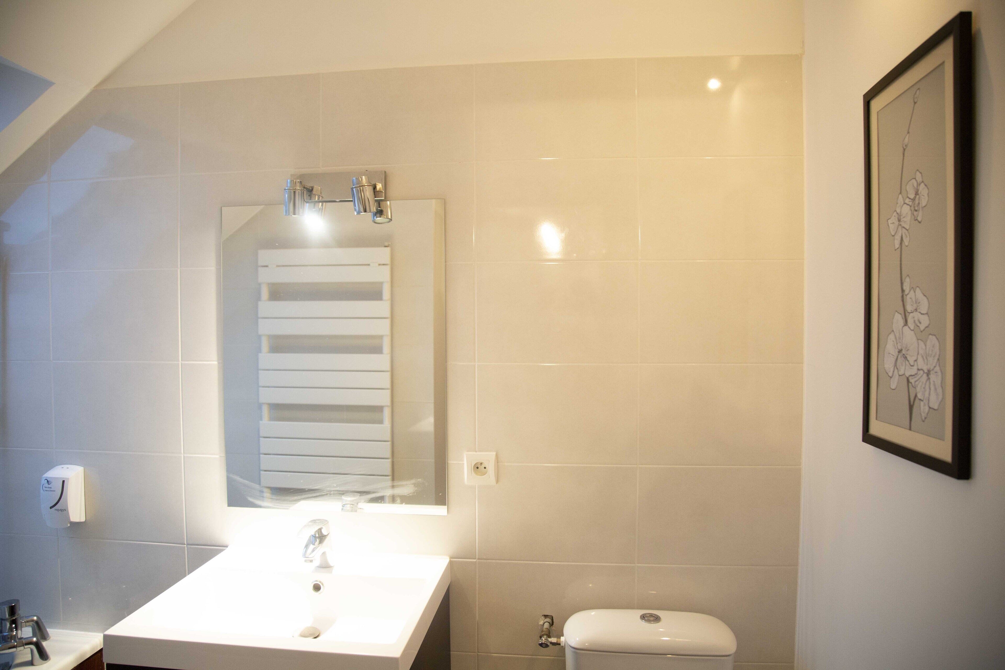 Un baño con lavamanos, espejo y retrete blancos.