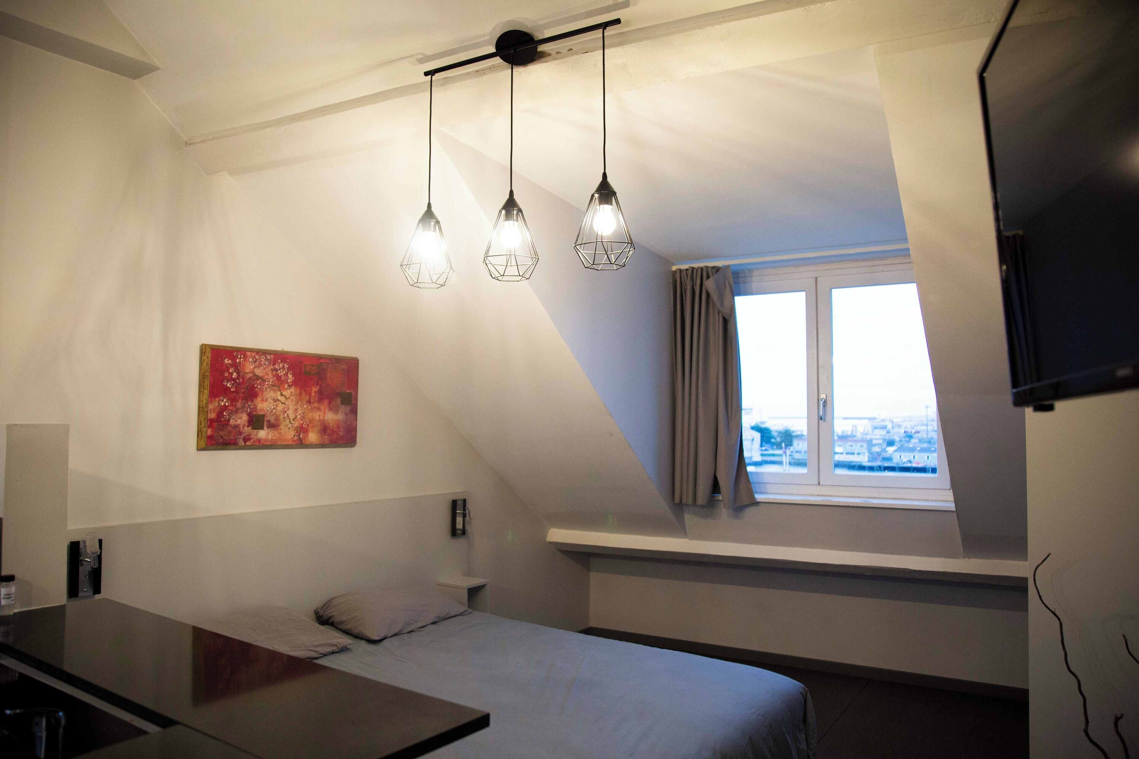 Un dormitorio con cama, escritorio, un cuadro y ventana con vistas.