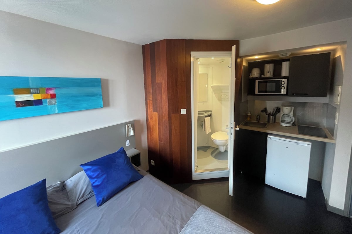 A compact hotel room with a bed, a small kitchenette, and a bathroom visible through an open door.