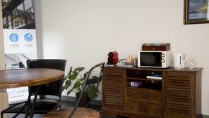 A room with a wooden cabinet, a microwave, a coffee maker, and a table with chairs. - Smart Appart Cherbourg La Rose des vents (Cherbourg-en-Cotentin)