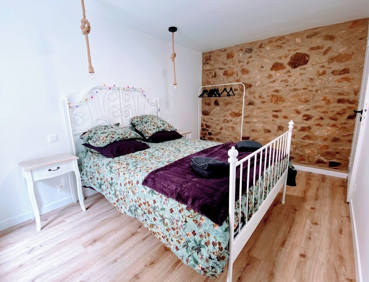 Ein Schlafzimmer mit einem Bett, einem Nachttisch, einer Hängelampe, einer Steinwand und einem Holzboden.