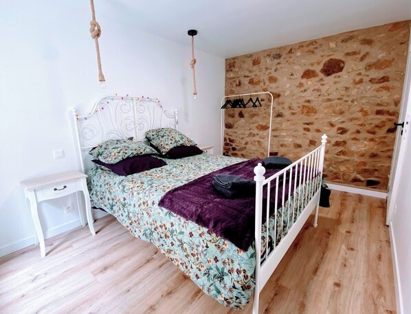 A bedroom with a bed, a bedside table, a hanging light, a stone wall, and a wooden floor. - Ty ker Iliz - beaches and small shops within walking distance! (Trélévern)