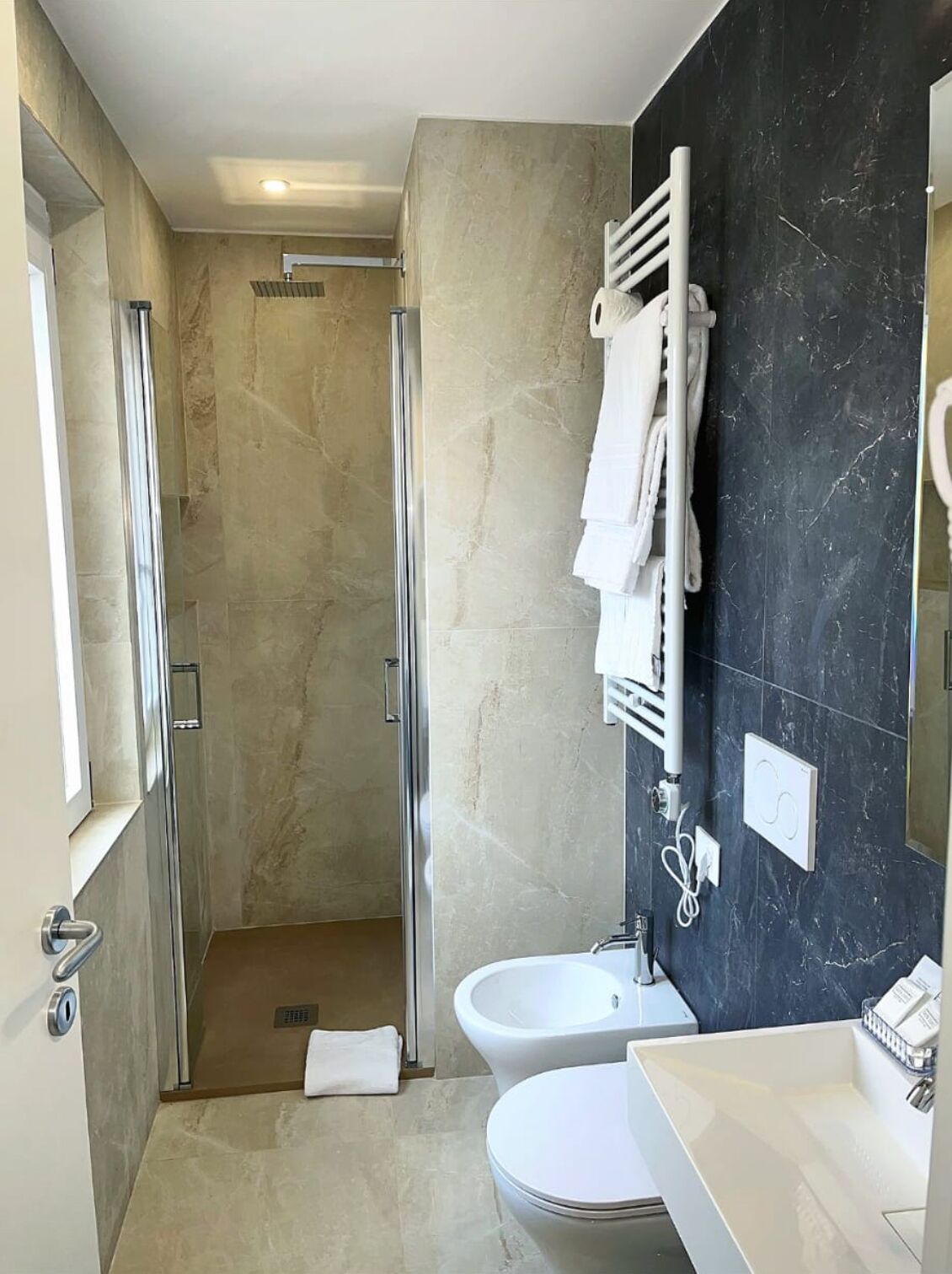 A modern bathroom with a glass-enclosed shower, a white sink, and a black marble wall.