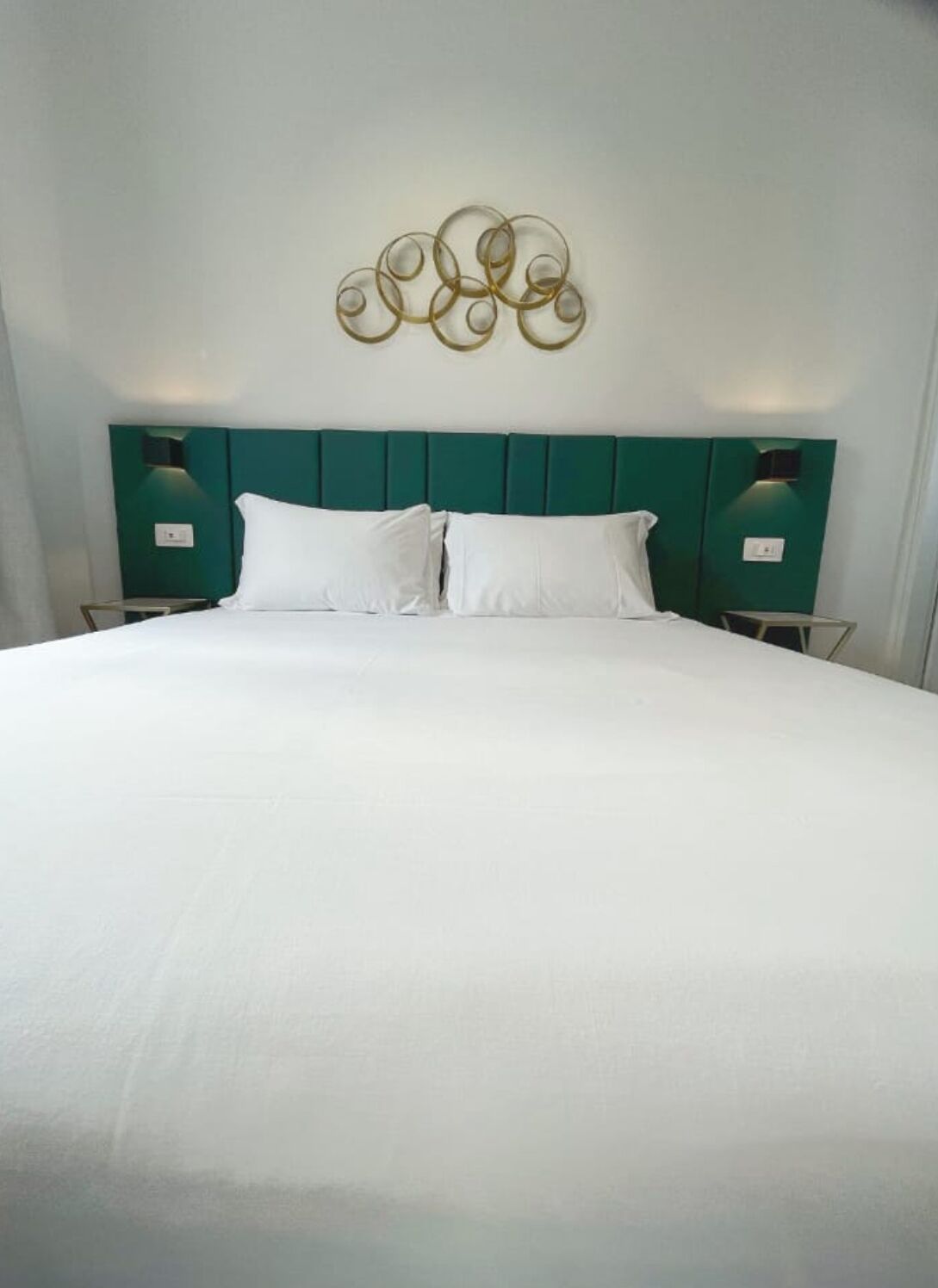 A neatly made bed with white linens, a teal headboard, and a wall-mounted decorative piece above it.