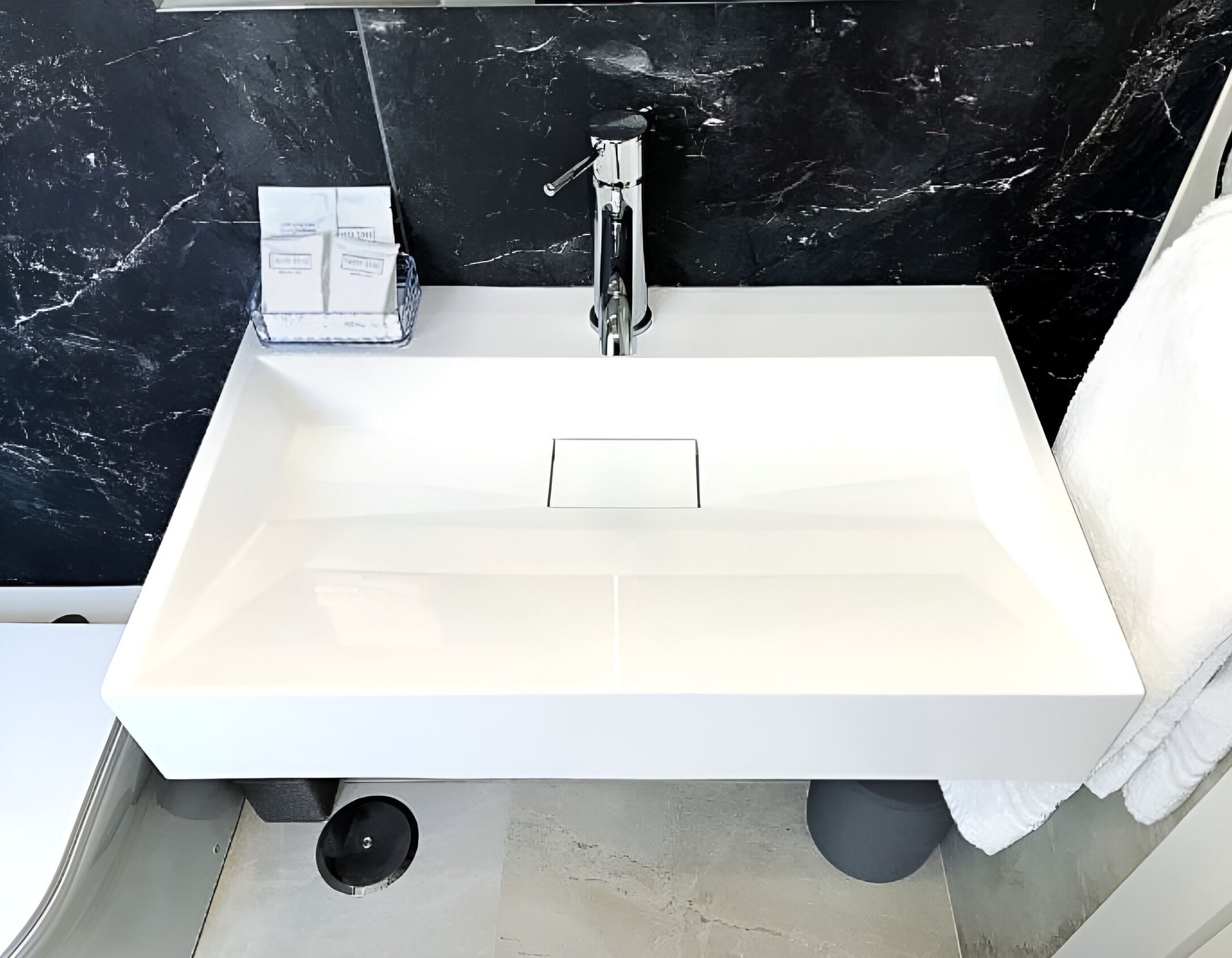 Et moderne badeværelse med en hvid vask, backsplash i sort marmor og en håndklædestang.