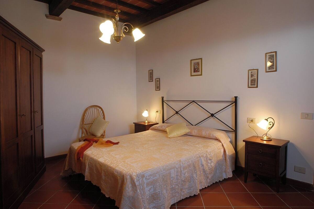 A bedroom with a bed, two bedside tables with lamps, a wooden wardrobe, and a chair.
