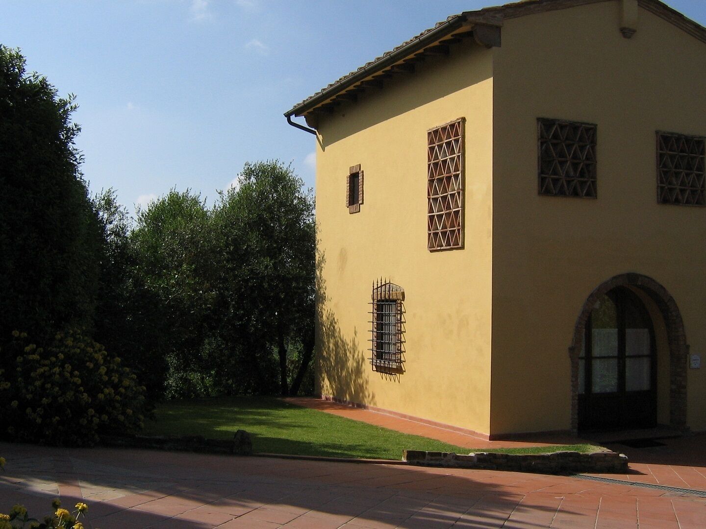 A building with a yellow facade, a tiled roof, and a small garden area with a pathway leading to the entrance.
