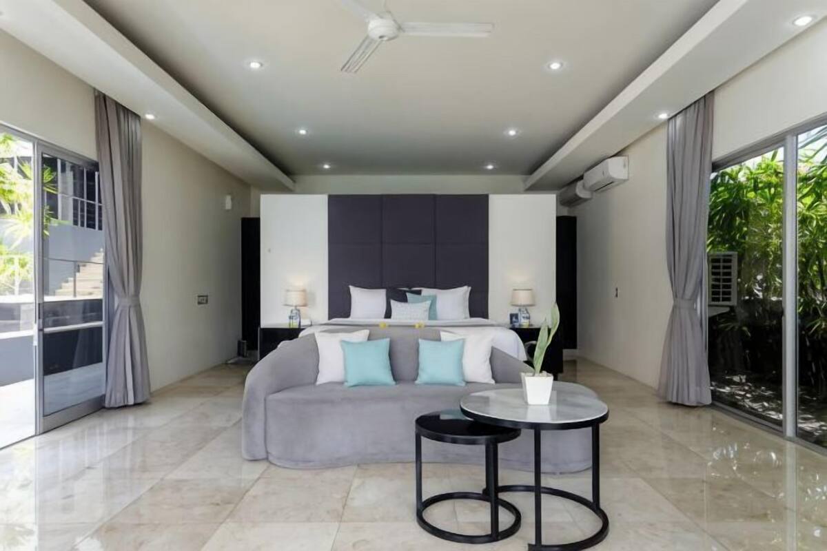 A modern bedroom with a bed, bedside tables, a round table, and a large window.