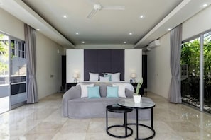 A modern bedroom with a bed, bedside tables, a round table, and a large window. - Suluban Cliff Bali Villa (Bali)