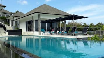 A swimming pool with lounge chairs and umbrellas, surrounded by a covered patio area.