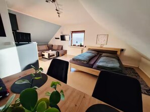 A compact, modern apartment with a loft-style bedroom, a dining area with a wooden table, and a kitchen area.