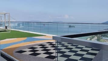 En balkong med ett rutmönstrat golv, ett glasräcke och utsikt över havet.
