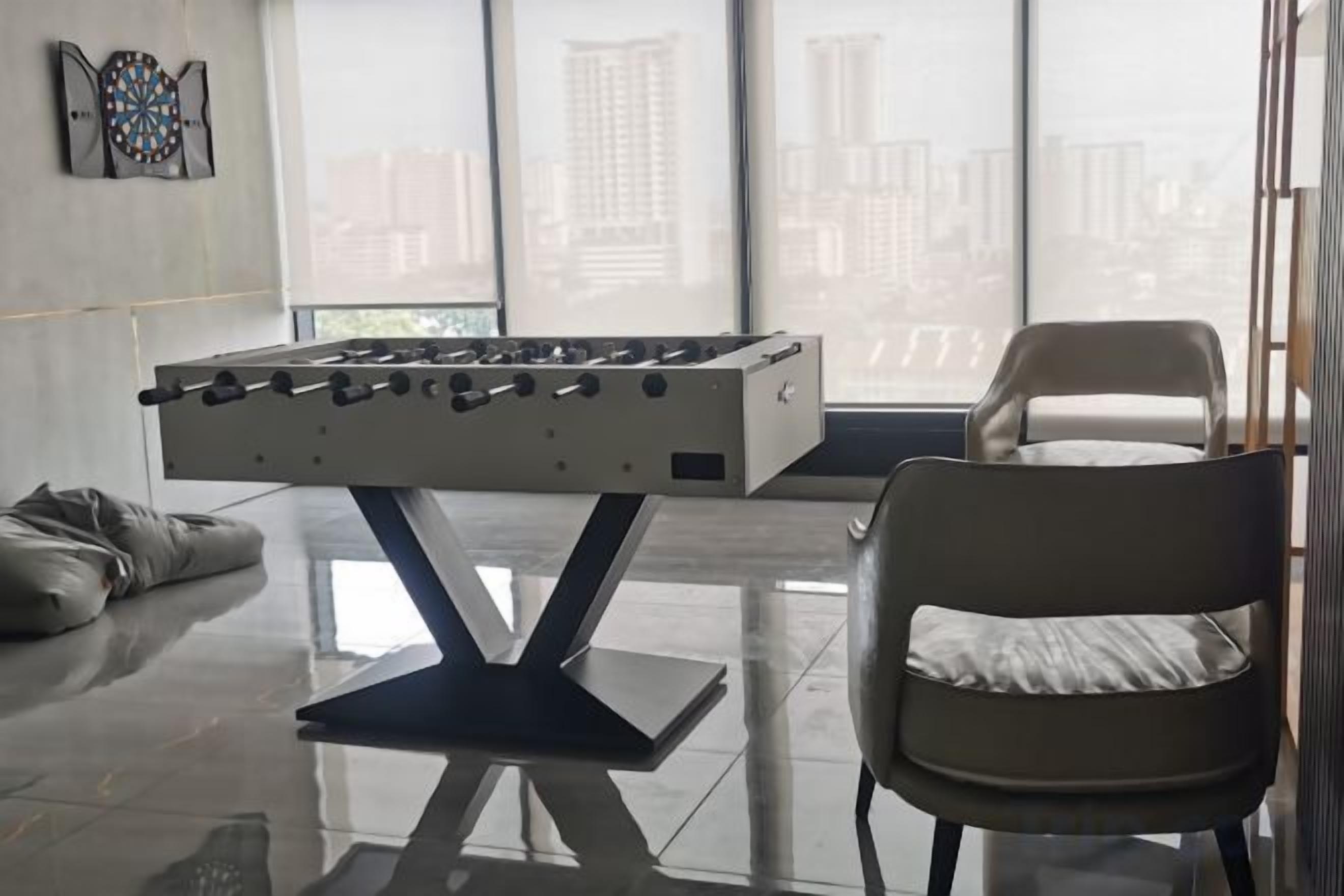 A foosball table in a modern room with a city view, a comfortable chair, and a sofa.