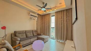 A living room with a sofa, ottoman, ceiling fan, and a large window with curtains.