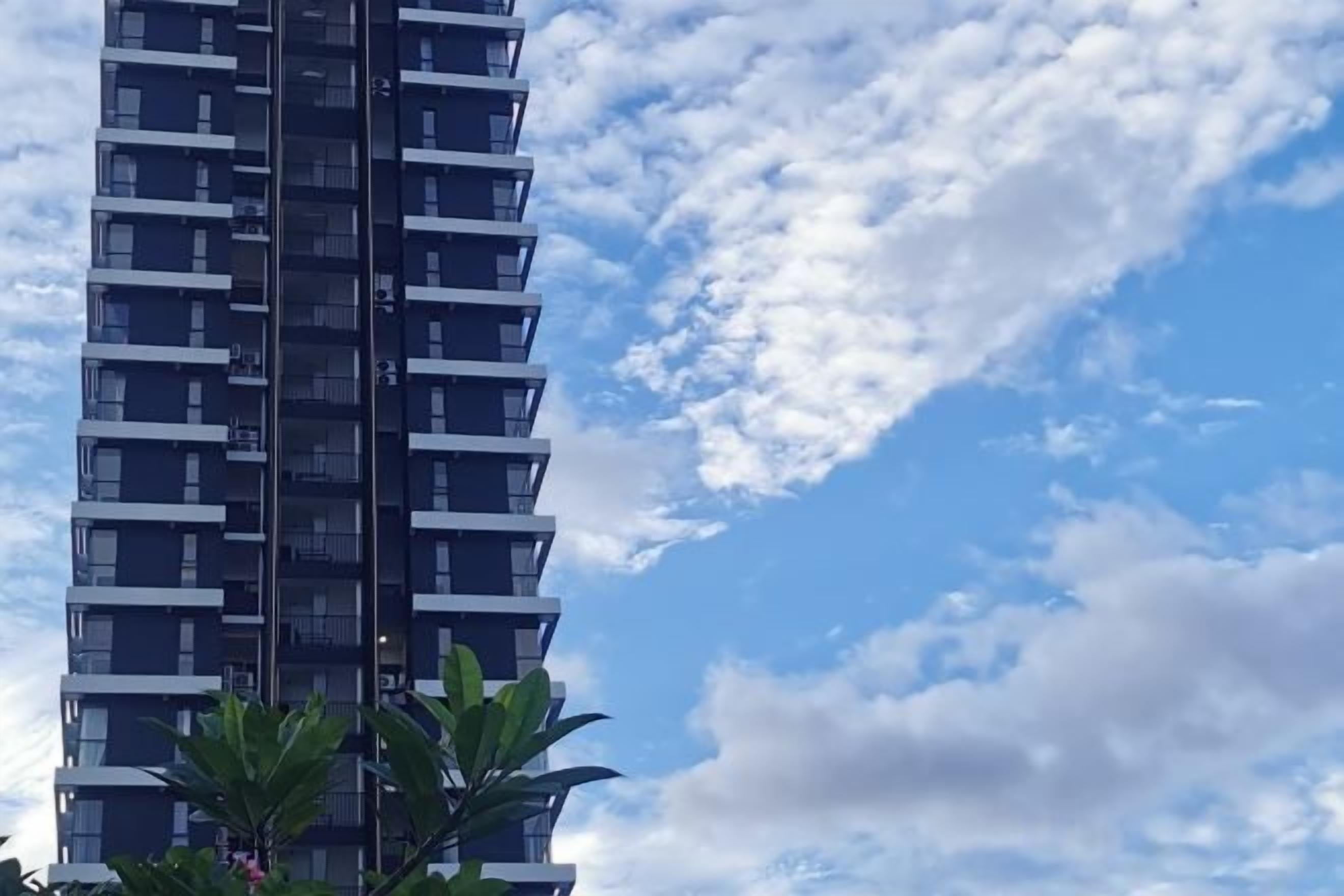 A tall building with multiple balconies and a clear sky with clouds.