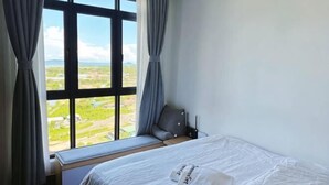 Habitación de hotel con cama, ventana con cortinas y vistas al campo, además de una mesita de noche.