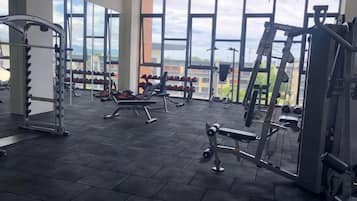 A gym with various exercise equipment, large windows, and a view of the outside.