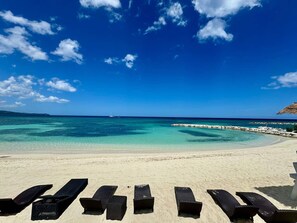 A beach with clear turquoise water, a sandy shore, and wooden lounge chairs. - Hospitality Expert SWF104 - Pool, Beach, Chef (Montego Bay)