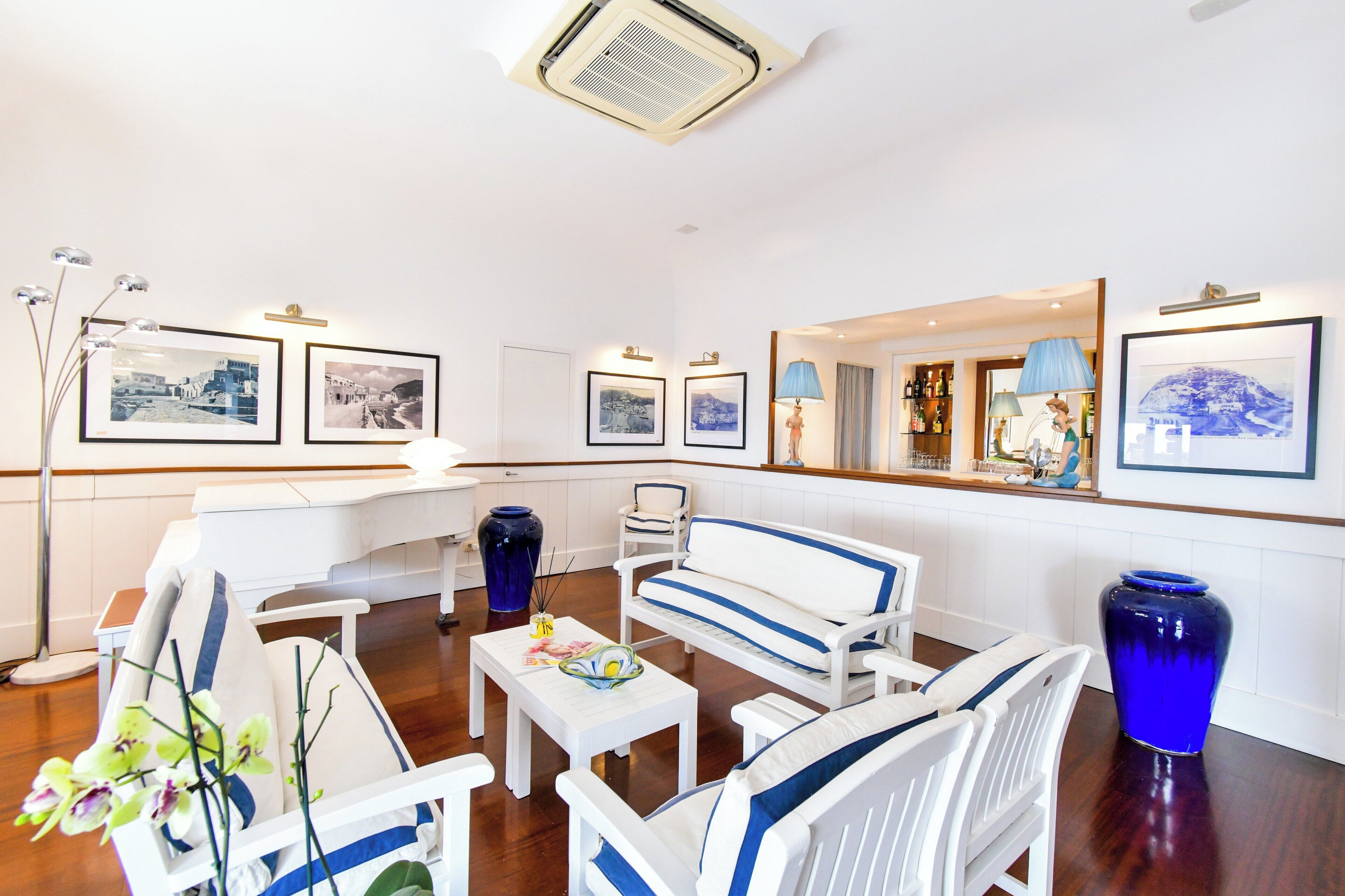 Un espace lounge moderne avec des meubles blancs et bleus, des tableaux encadrés aux murs et un coin bar avec des bouteilles et une lampe.