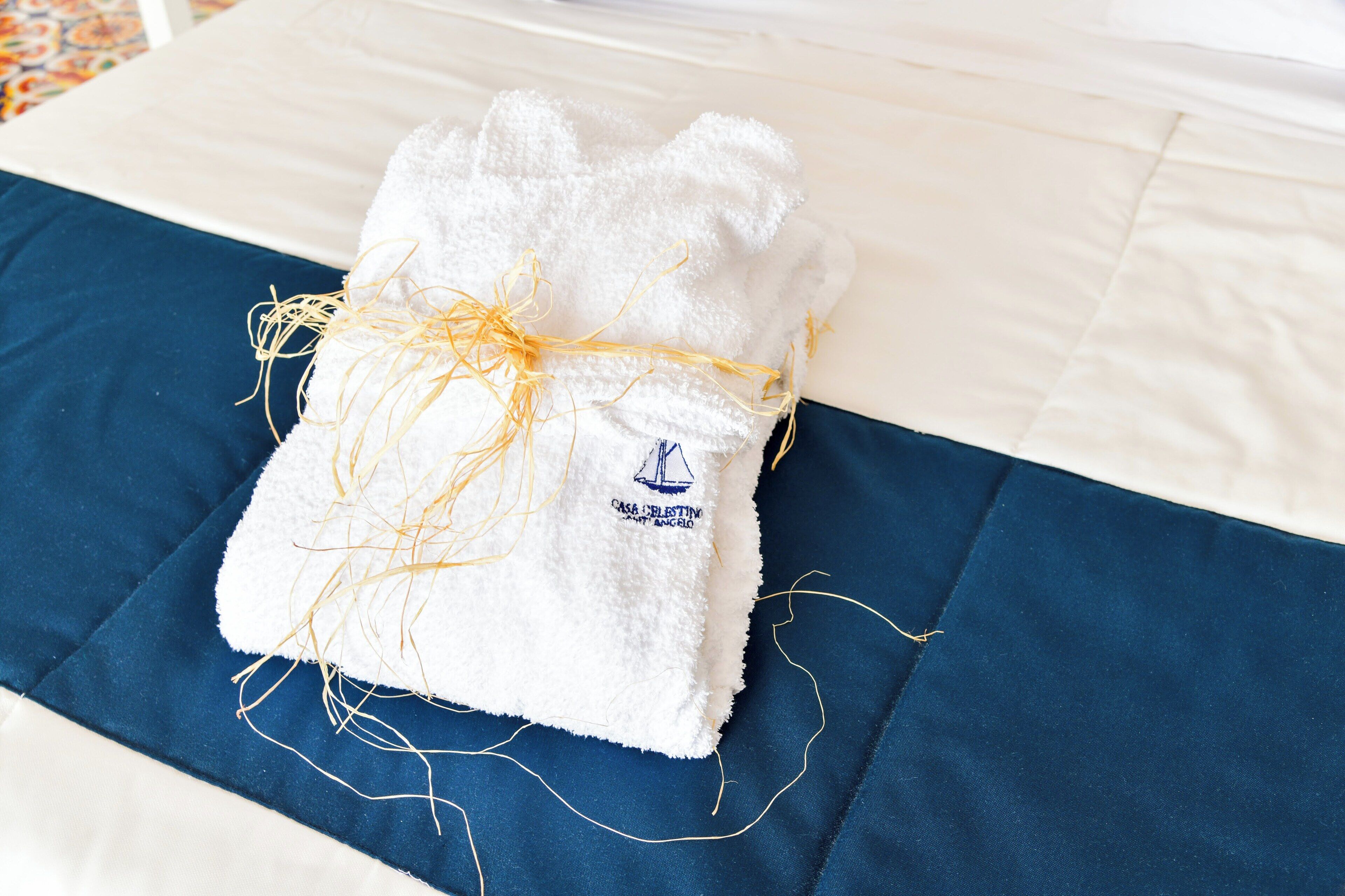 A white towel tied with a yellow string on a bed with a blue bedspread.