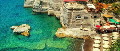 Un hôtel en bord de mer, avec une structure construite à flanc de falaise, des eaux d’un bleu limpide et des espaces de détente en plein air.
