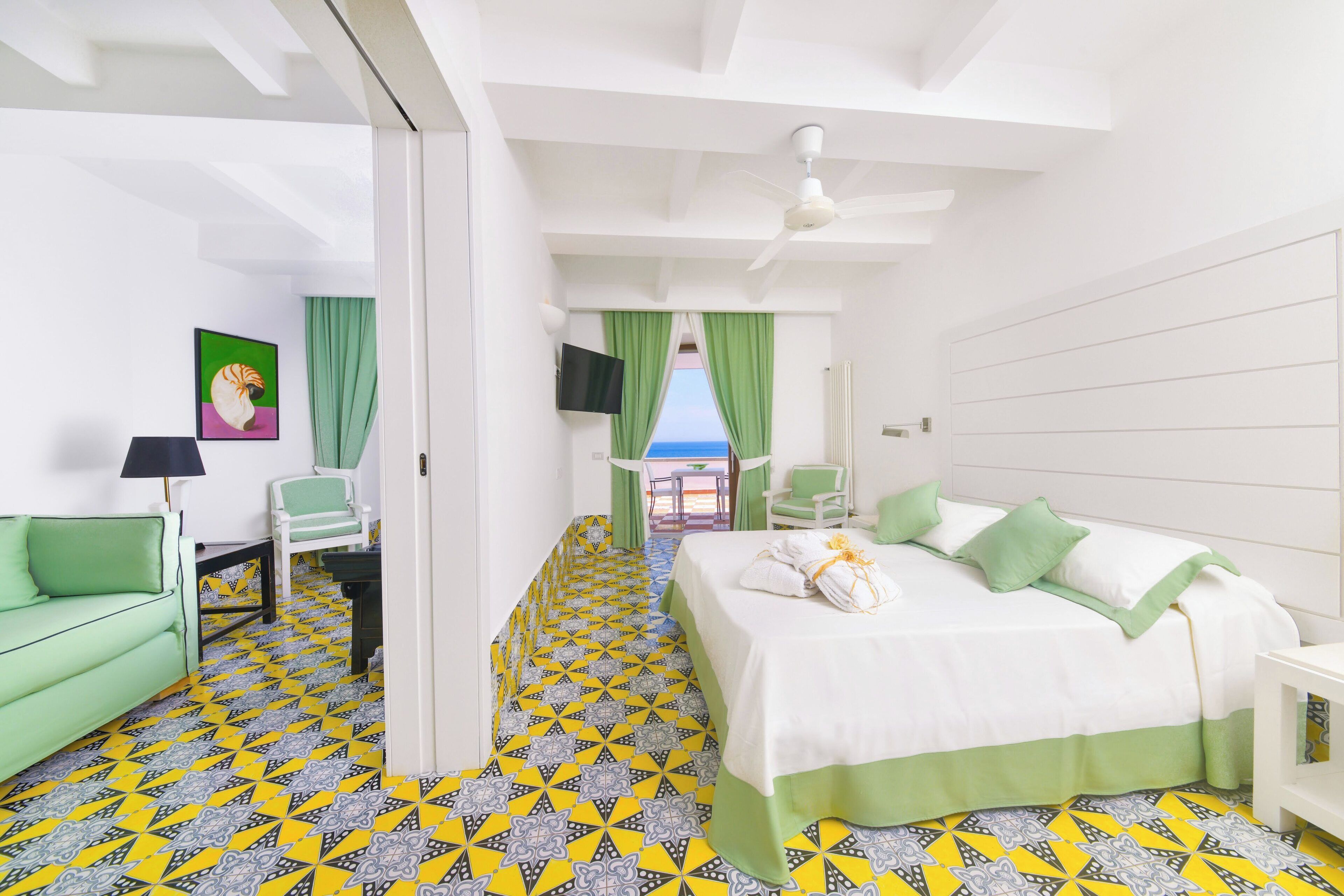 A hotel room with a bed, a green sofa, a TV, and a view of the sea.