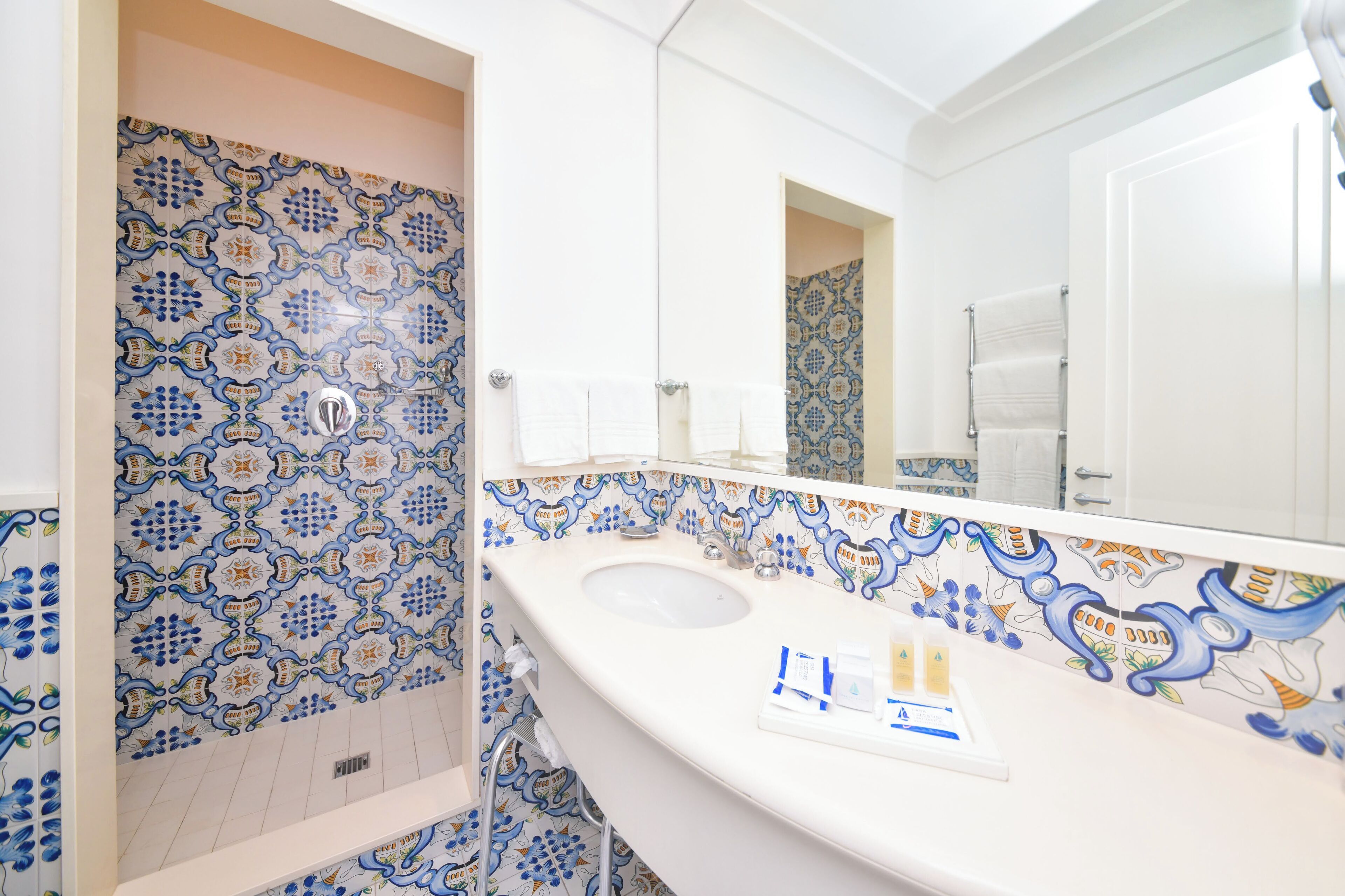 Un baño con lavamanos blanco, un espejo y baldosas estampadas.