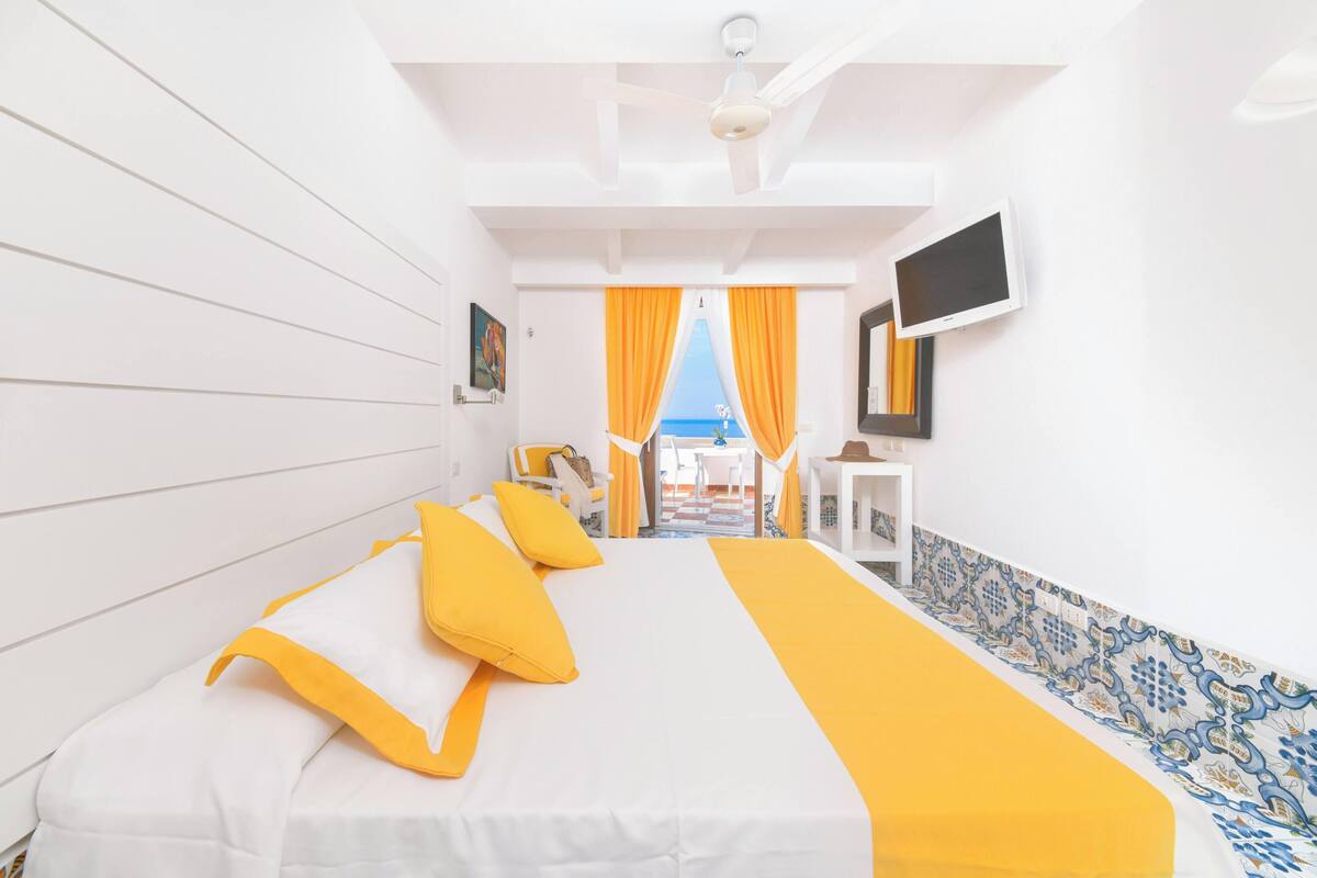Une chambre d’hôtel avec un lit, une télévision et une vue sur la mer, visible à travers les rideaux.