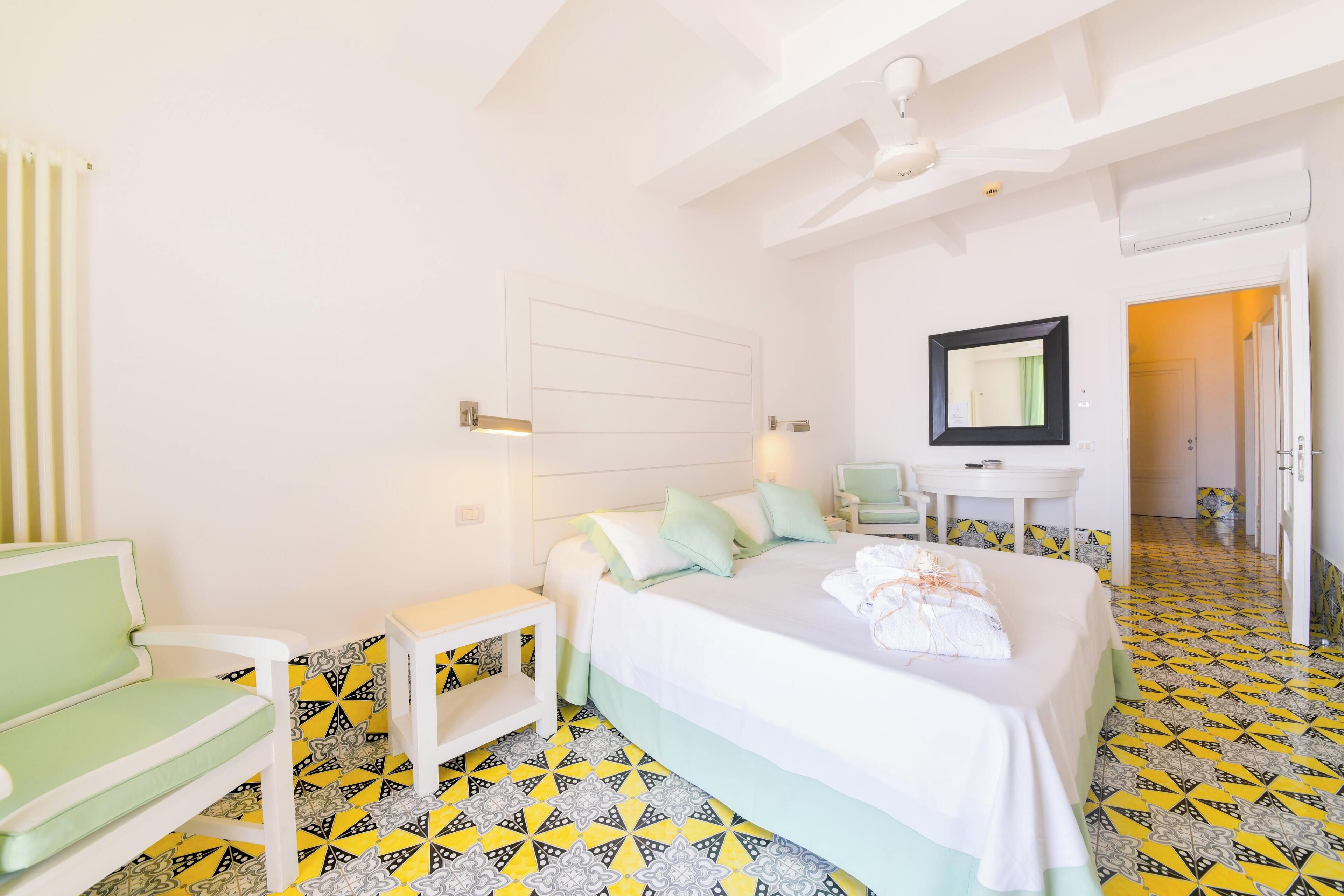 A hotel room with a bed, a chair, a small table, and a mirror.