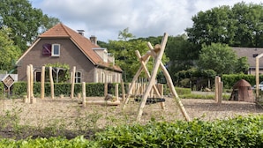A garden with wooden play structures, a brick house, and a small dome structure. - Holiday Home in Plasmolen Near Nature Reserves (Plasmolen)