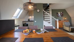 A dining area with a wooden table, a bowl of fruit, and a magazine. There is a staircase leading to an upper level. - Holiday Home in Plasmolen Near Nature Reserves (Plasmolen)