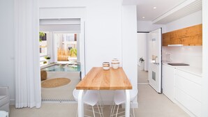A modern kitchen with white cabinetry, a wooden dining table, and two white chairs. - Almyra Luxury Pool Suite with Private Pool (Πάνορμος)