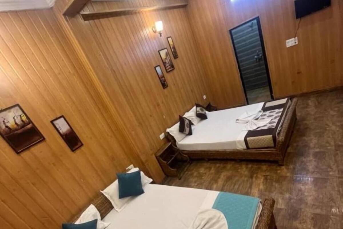 A hotel room with two beds, wooden paneling, a ceiling fan, and a wall-mounted TV.