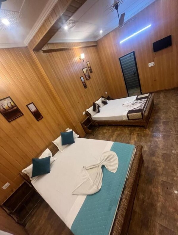 A hotel room with two beds, wooden paneling, a ceiling fan, and a wall-mounted TV.