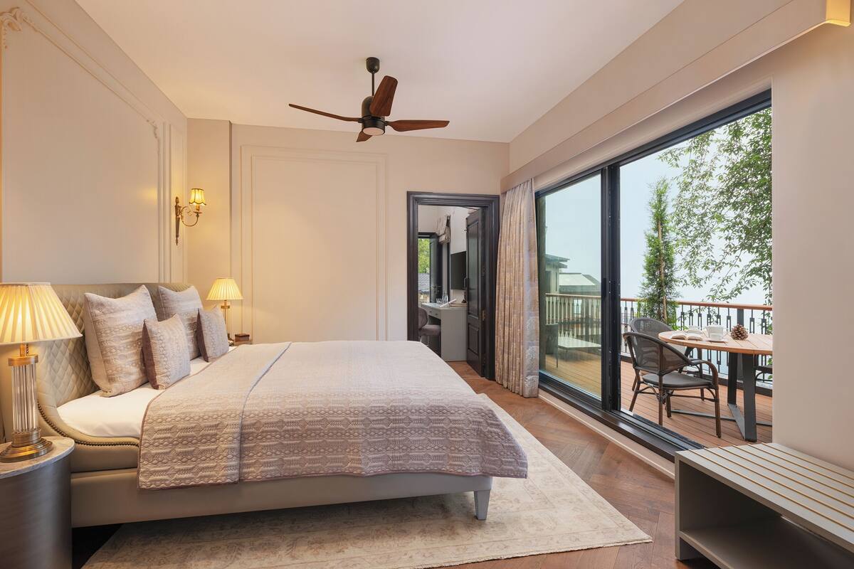 Un dormitorio amplio con una cama grande, ventilador de techo y balcón con mobiliario exterior.