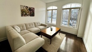 En stue med en beige sofa, et træ sofabord og et stort vindue med udsigt.
