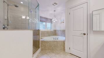 A modern bathroom with a glass shower enclosure, a freestanding bathtub, and a white door.