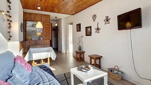 Et hyggeligt rum med trælofter, en seng, en sofa, et lille bord og et fjernsyn monteret på væggen.