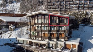 Et flere-etagers hotel med balkoner, et skiområde i baggrunden og et snedækket område.