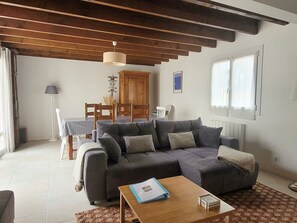 Un salon comprenant un canapé, une table basse, une table à manger avec des chaises, un meuble en bois et une fenêtre avec des rideaux.