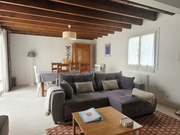 Una sala de estar con sofá, mesa de centro, mesa de comedor con sillas, aparador de madera y ventana con cortinas.