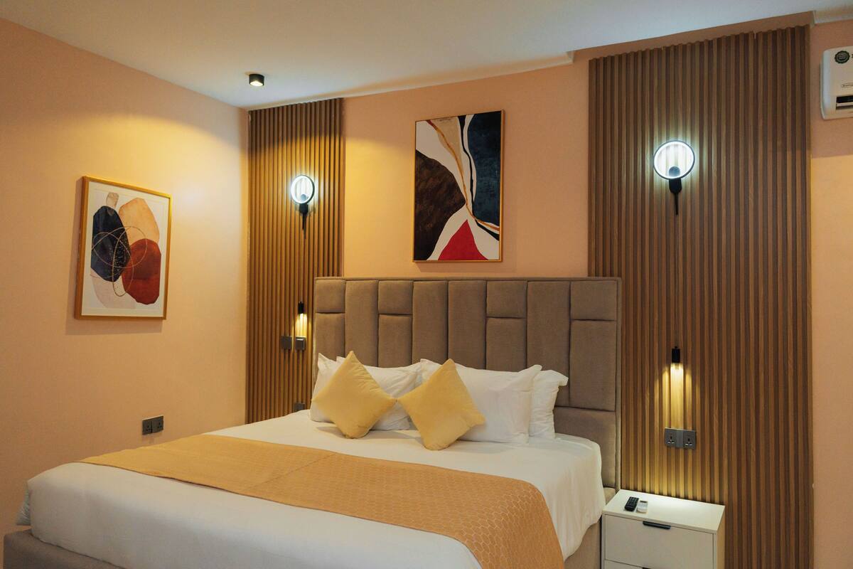 A hotel room with a large bed, a bedside table, a wall-mounted light, and a painting.