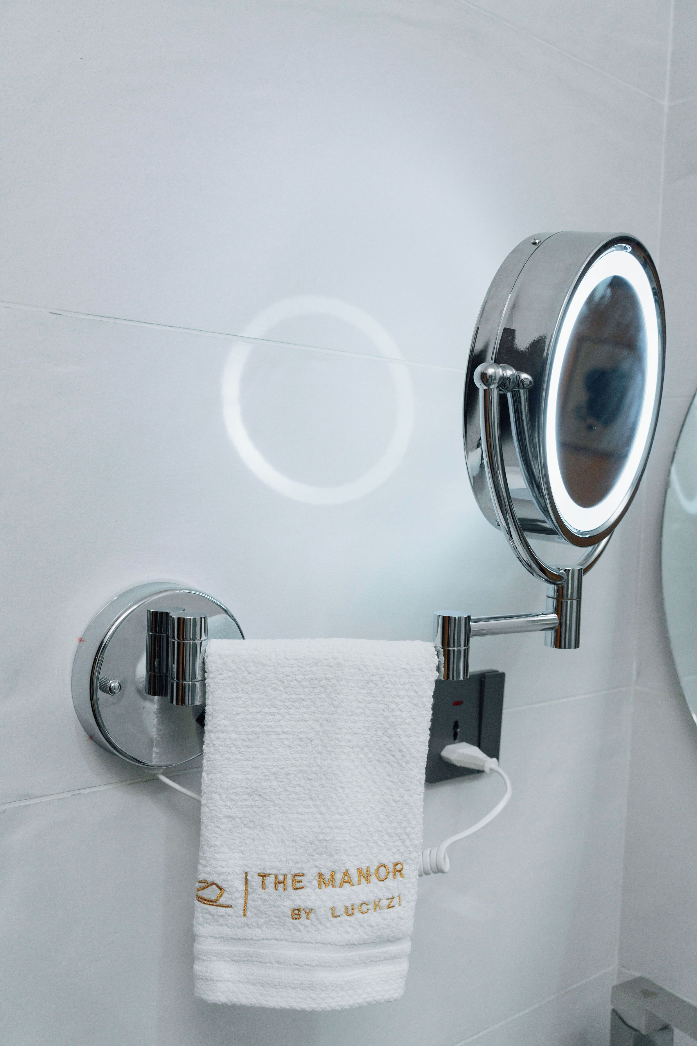 A bathroom with a white towel hanging on a wall-mounted towel rack, a round mirror, and a towel warmer.